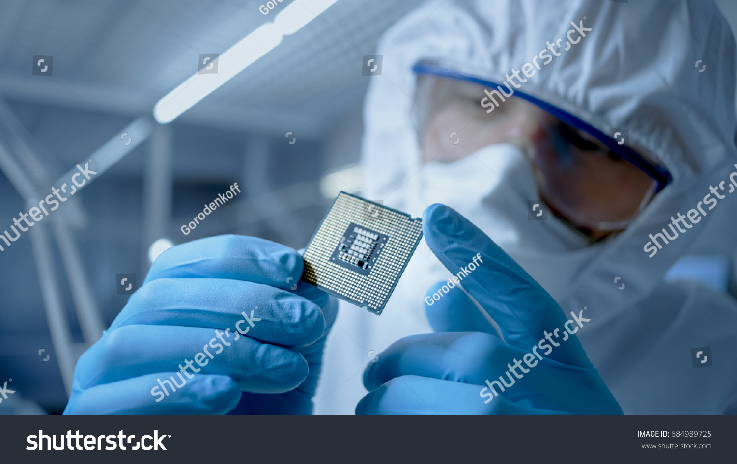 In Ultra Modern Electronic Manufacturing Factory Design Engineer in Sterile Coverall Holds Microchip with Gloves and Examines it. #684989725