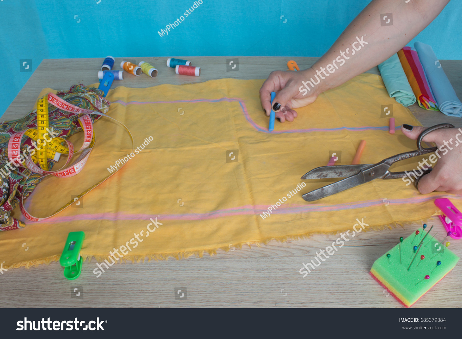 Close up of  woman's hands drawing a pattern on yellow tissue. Measuring tape and sewing accessories. A tailor is laying out a dress/Sewing layout #685379884
