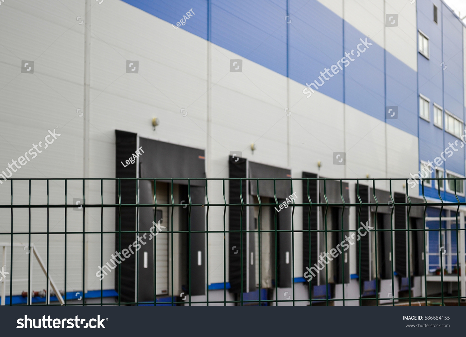 Large distribution warehouse in the background behind a latticed fence #686684155