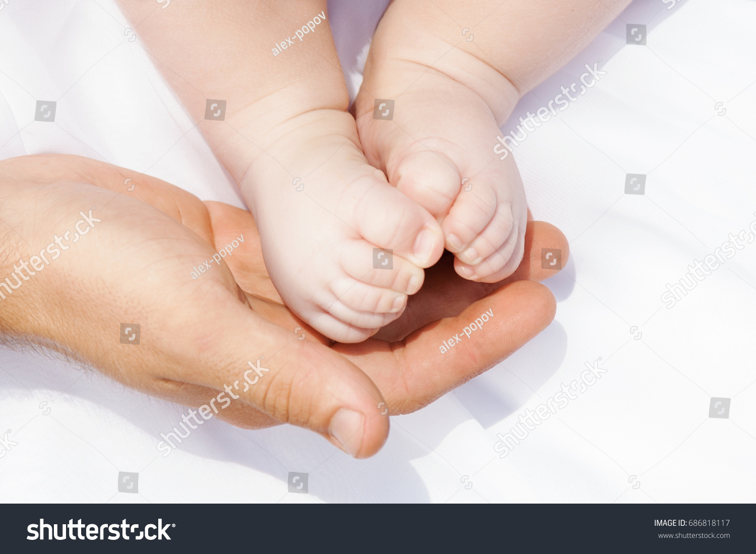The legs of the child on the father's hands. Little Newborn Baby's feet on male Shaped hands on the white background.Sensual conceptual image of fatherhood. Concept of happy family #686818117
