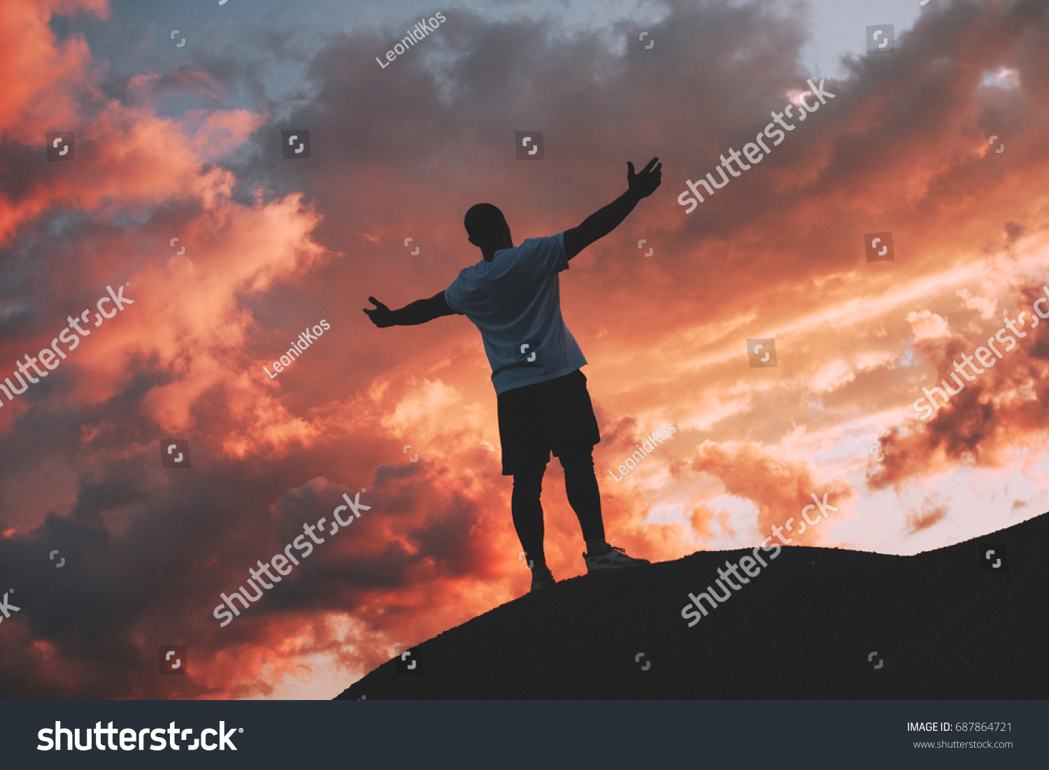 Successful and happy male athlete stands with his arms raised to the sunset #687864721