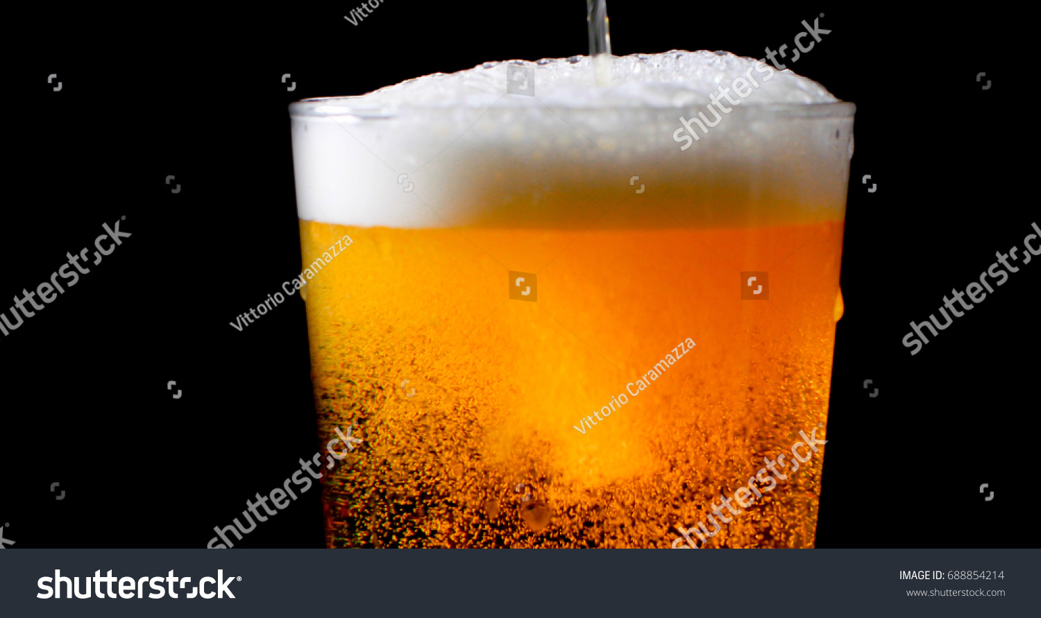 Pouring lager beer on a pint glass with black background #688854214