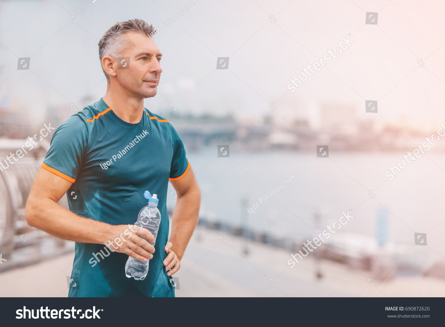 Portrait of healthy athletic middle aged man with fit body holding bottle of refreshing water, resting after workout or running. middle aged male with a drink after outdoor training.  #690872620