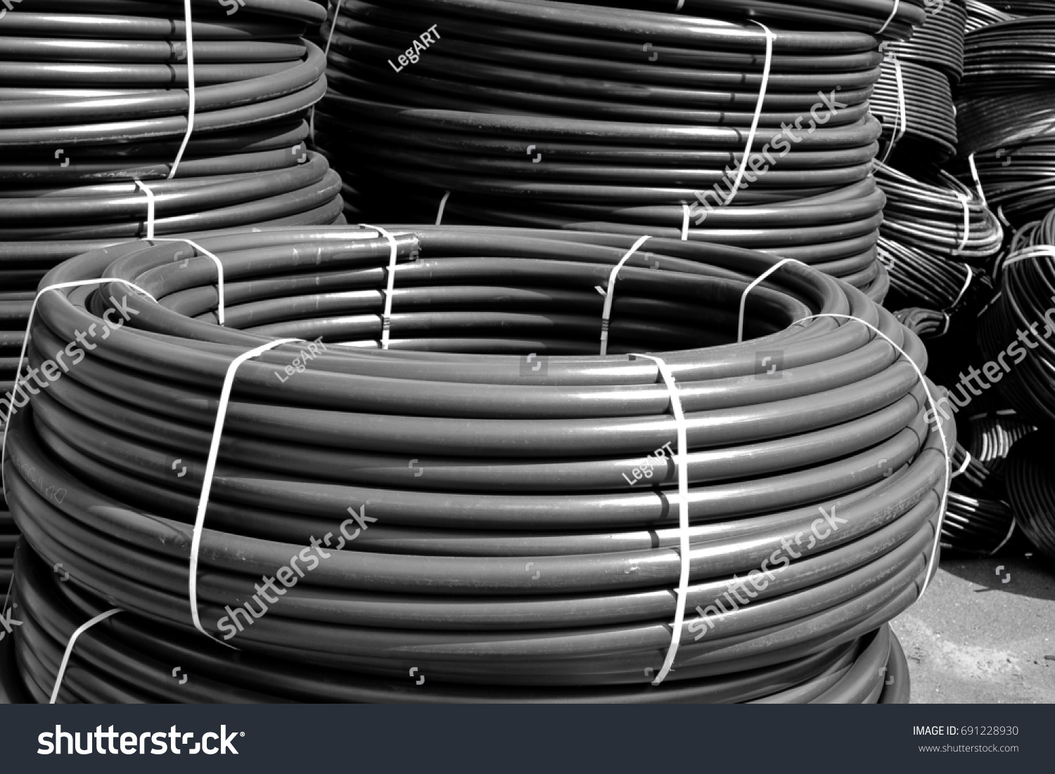 Coiled black plastic pipes stored outdoors #691228930