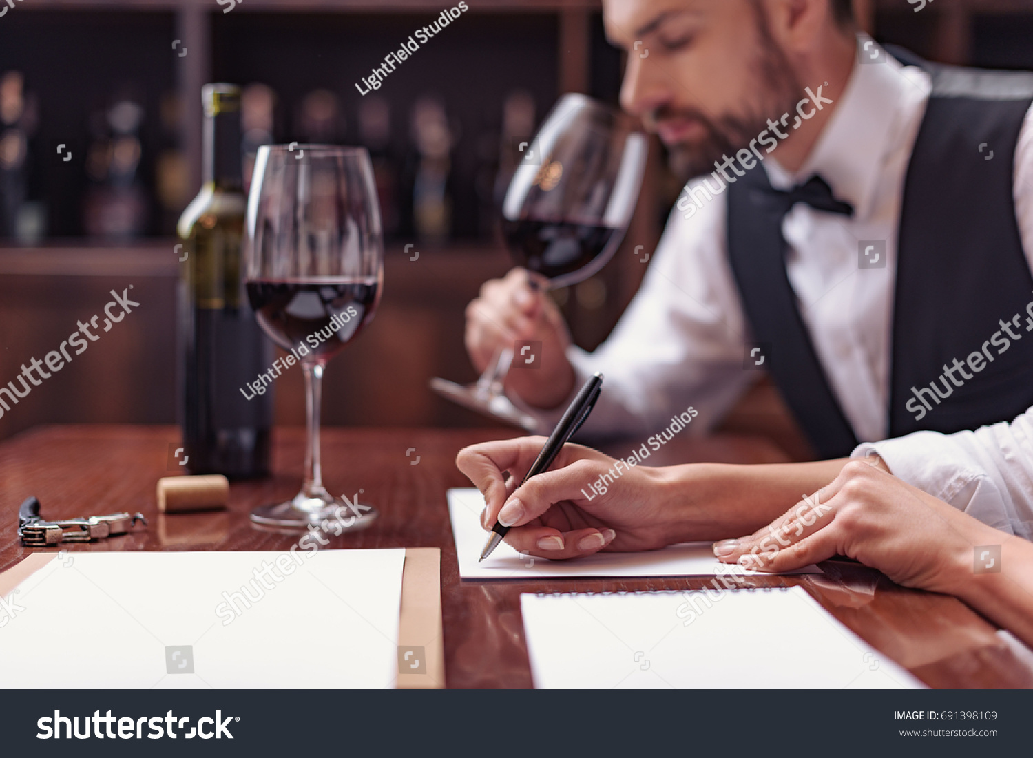 Two sommeliers, male and female tasting red wine and making notes at degustation card #691398109