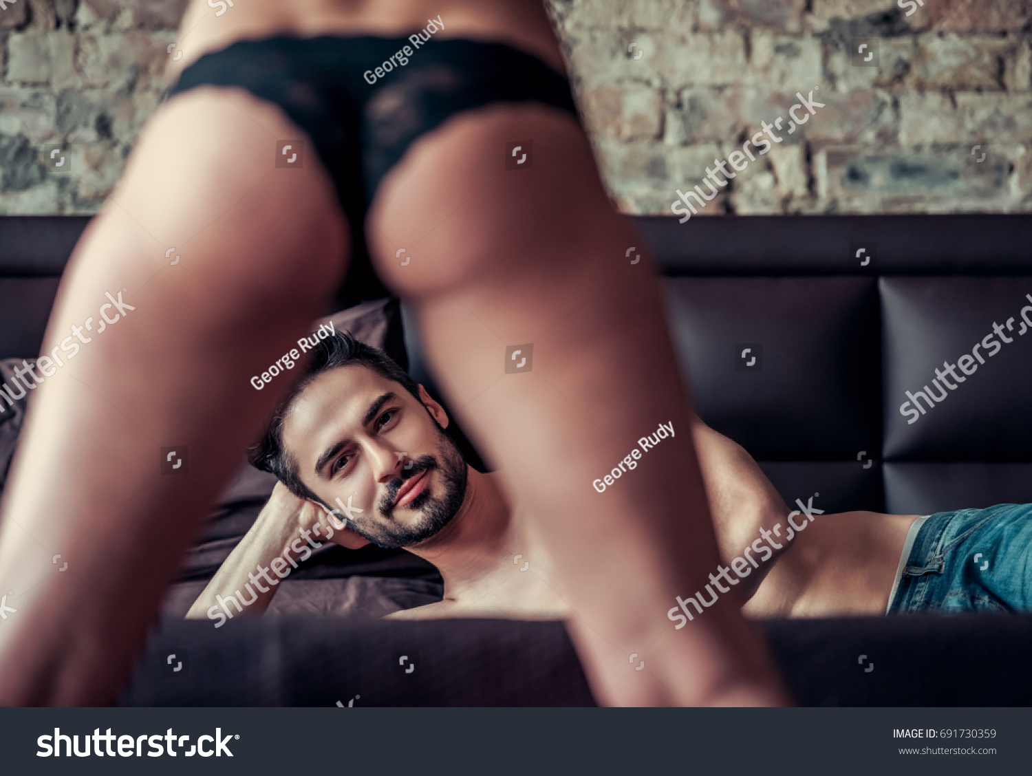 Couple having sex. Handsome man is lying on bed and looking at camera between woman's legs #691730359