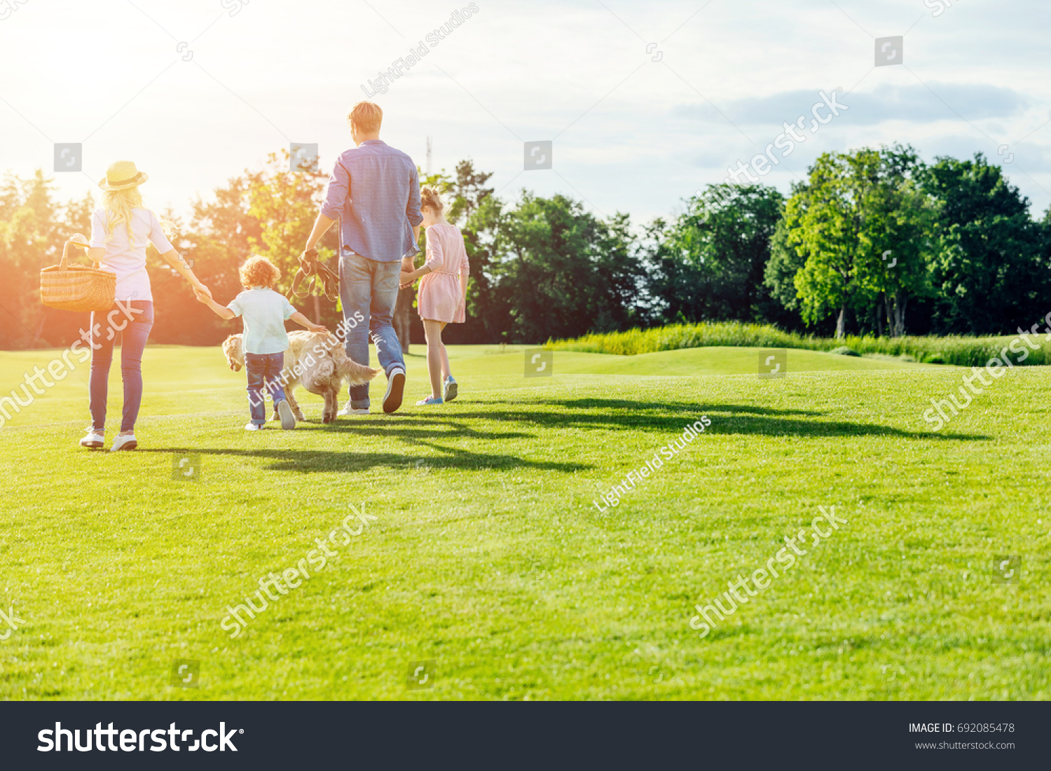 back view of family with pet walking on green meadow in park #692085478