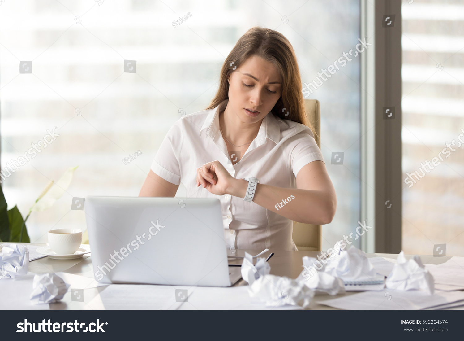 Busy punctual businesswoman checking time to deadline, looking at wristwatch while working with laptop and documents, need to finish work on time, counting on overtime bonus, waiting workday ending #692204374