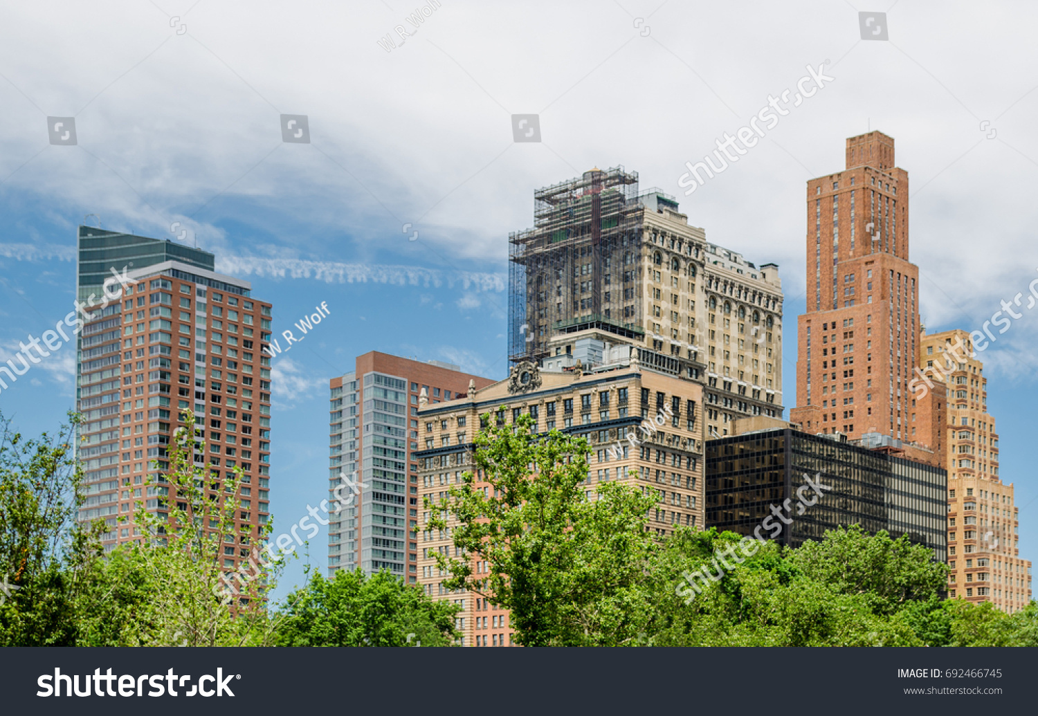 Buildings with blue sky and clouds with summer trees at base. #692466745