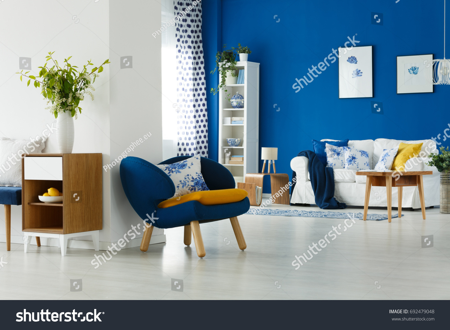Blue armchair with mustard pillow by the white wall in lounge #692479048