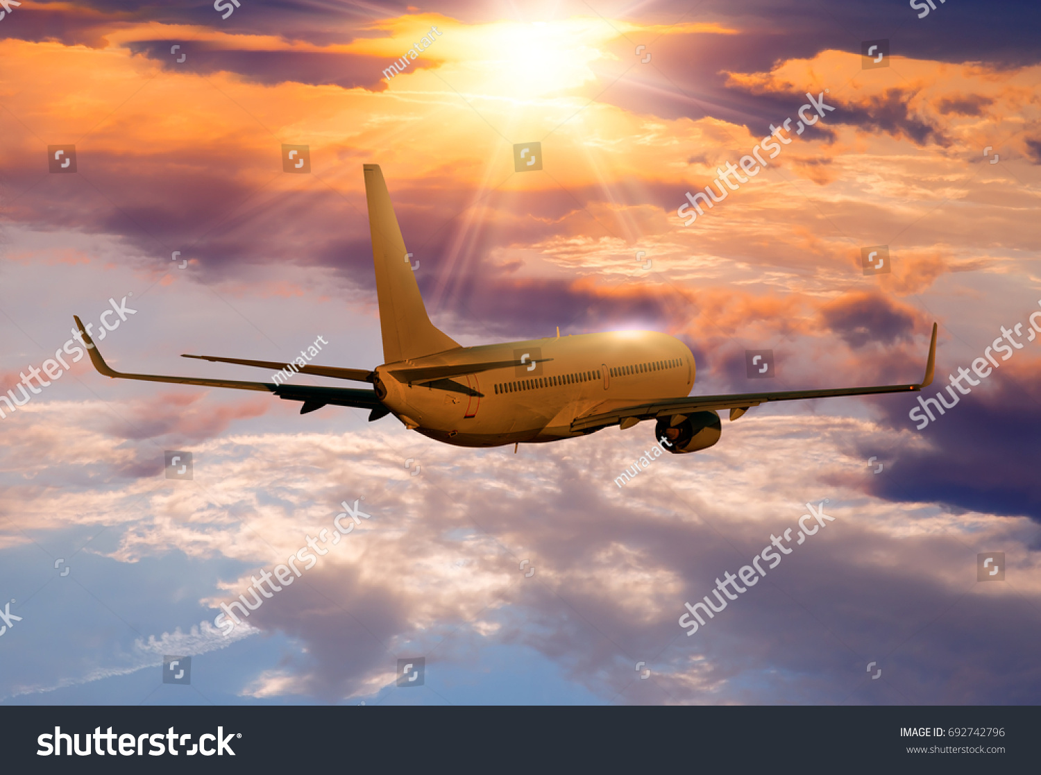 Commercial airplane flying above clouds in dramatic sunset  #692742796