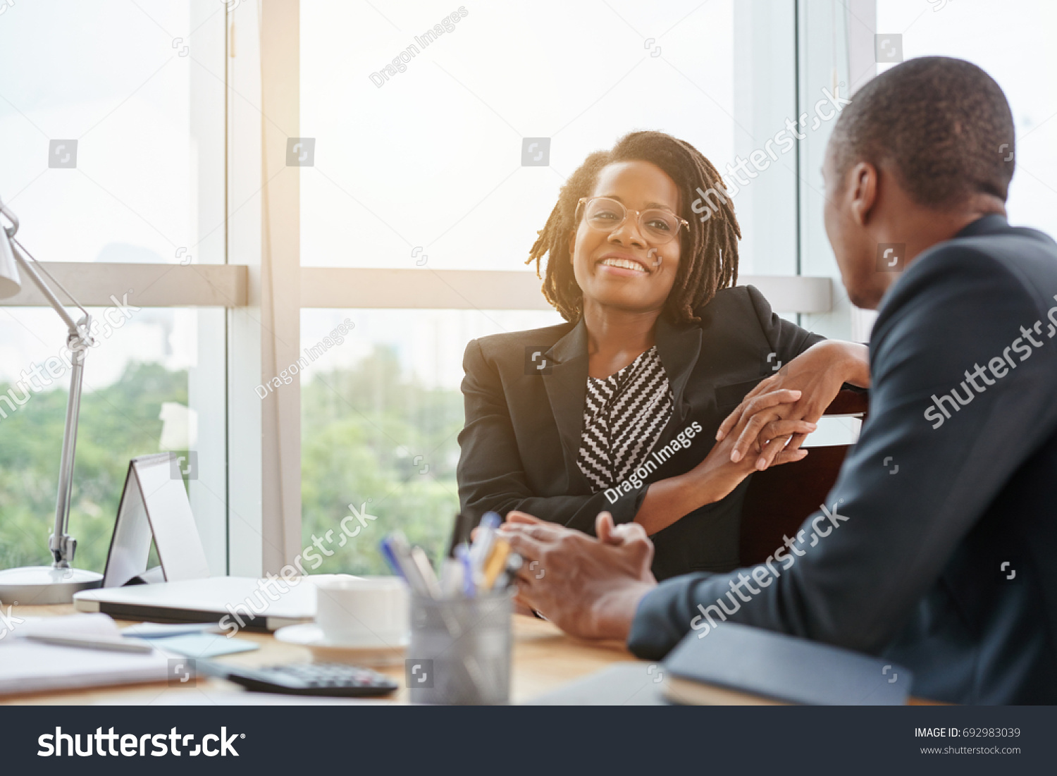 Beautiful smiling African-American business lady chatting with coworker #692983039