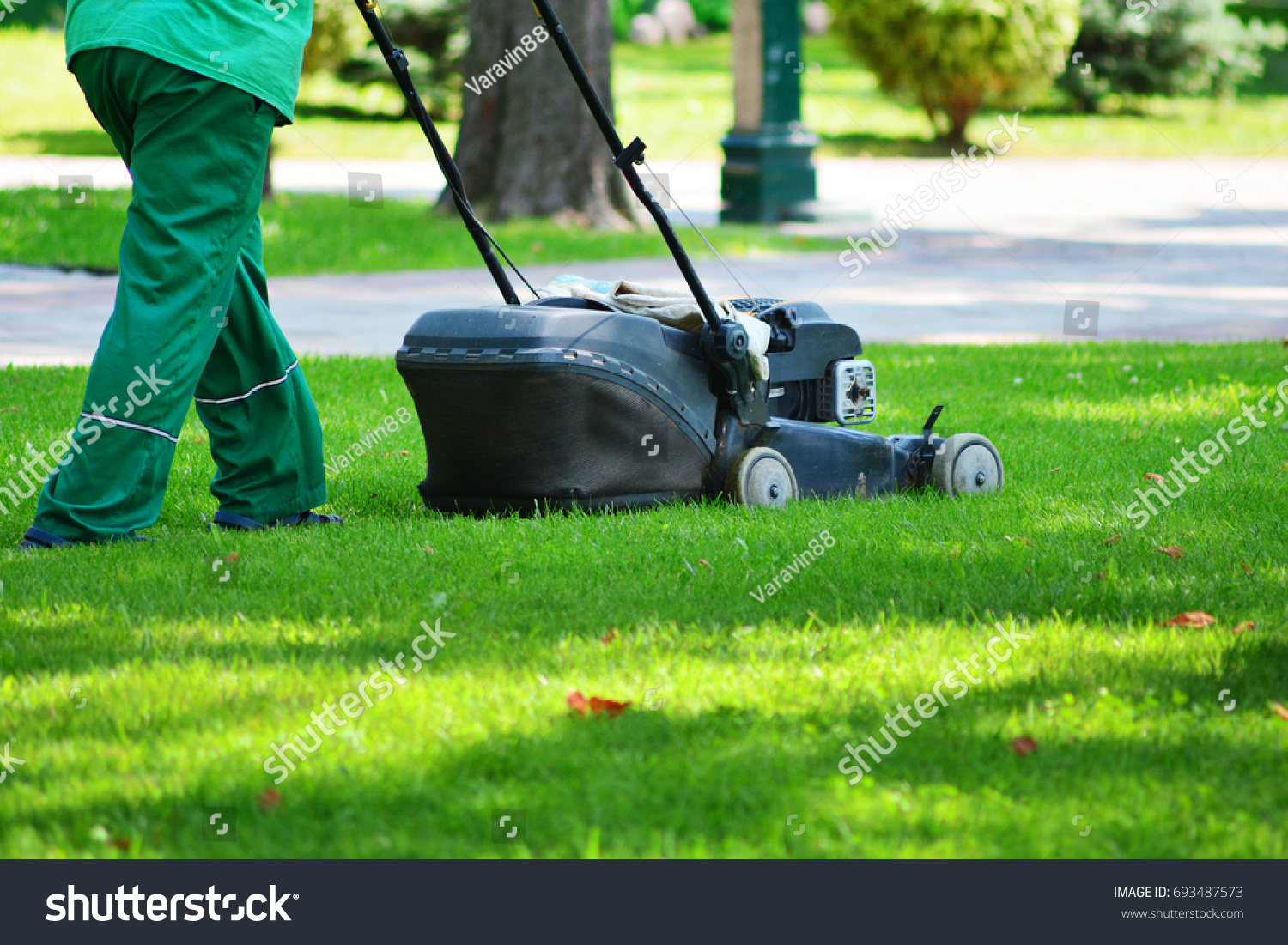 A garden worker takes on a lawn with a lawn mower. Lawn mowing. #693487573