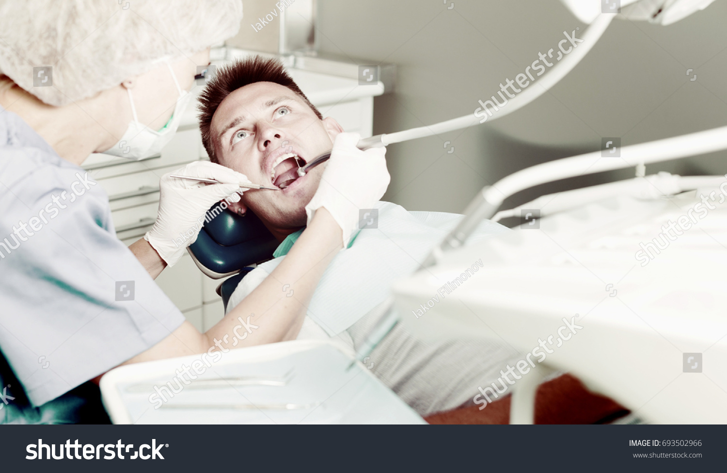 Male patient sitting on chair in dental office getting dentist treatment #693502966