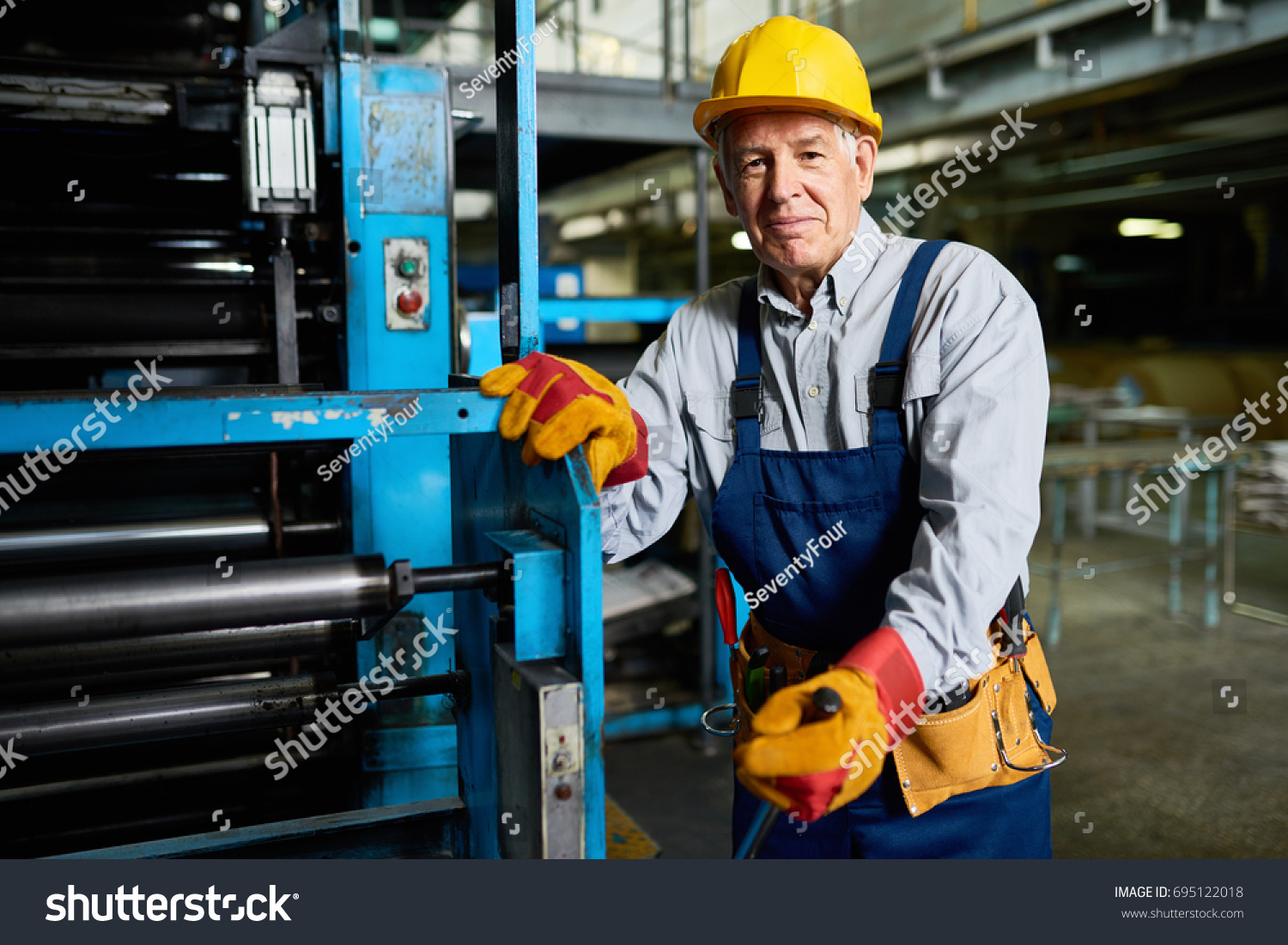 Portrait of senior factory worker smiling looking at camera standing by machine in modern industrial workshop #695122018