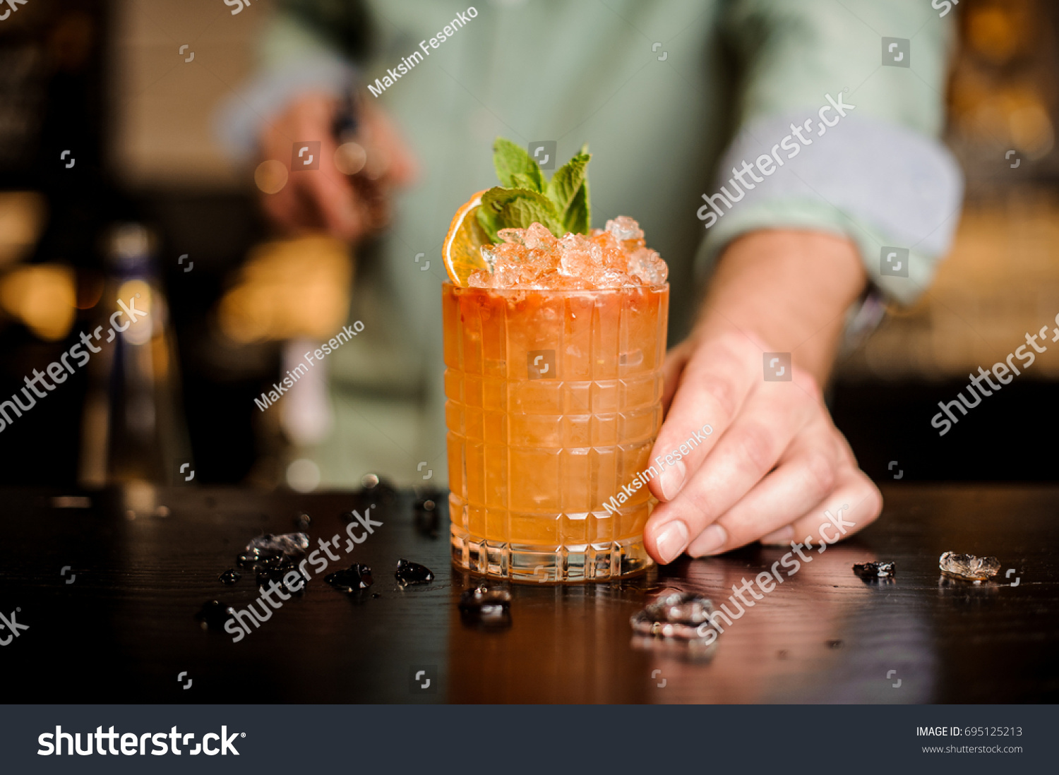 Bartender finished decorating his cocktail with mint and orange slice #695125213