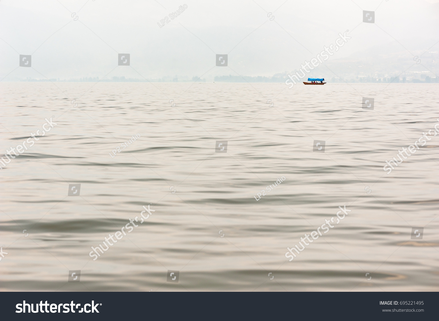 Small boat on a lake in the haze with mountains in the background #695221495