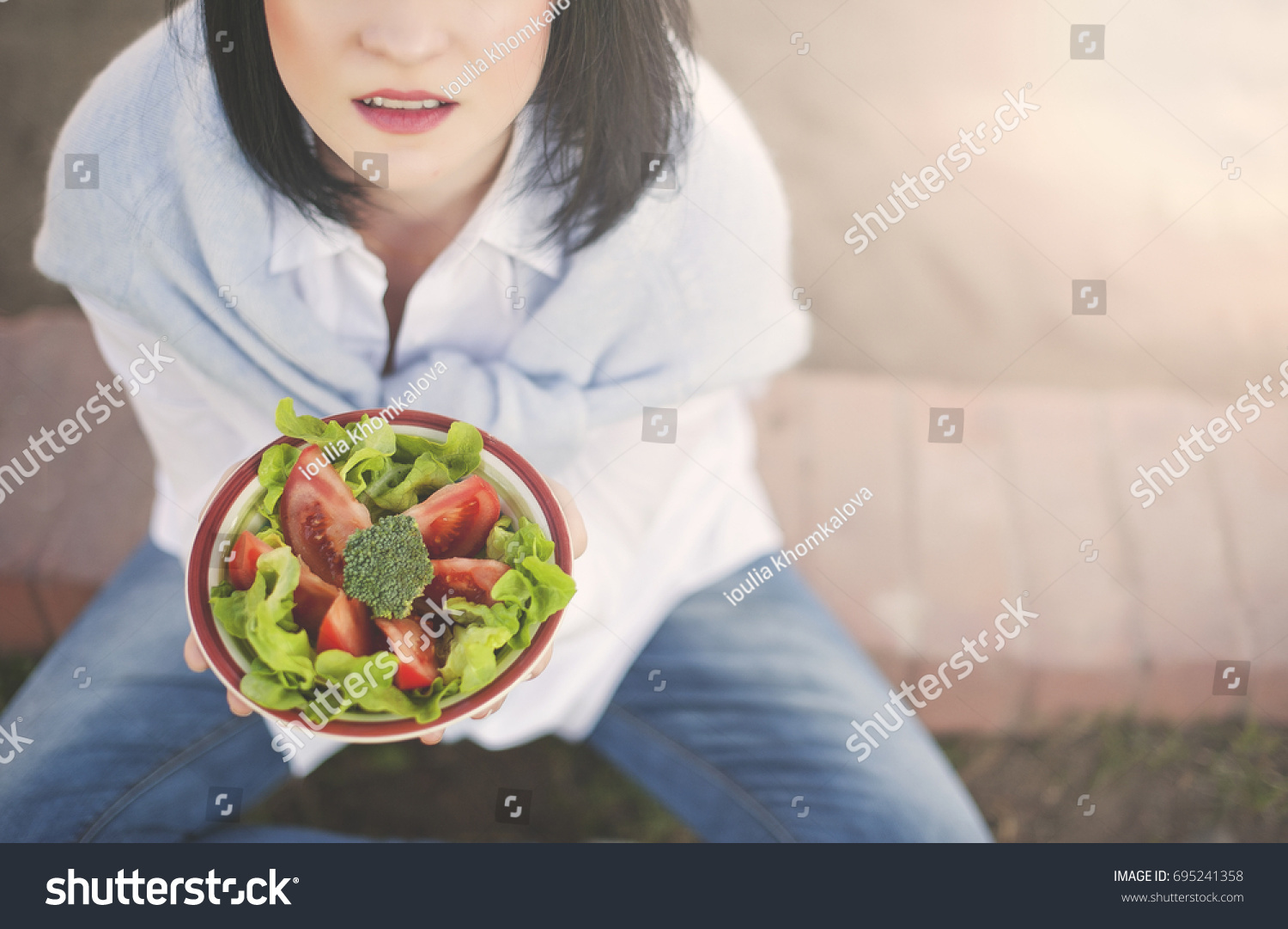 Young woman sitting on the green grass, winks and eating green salad #695241358