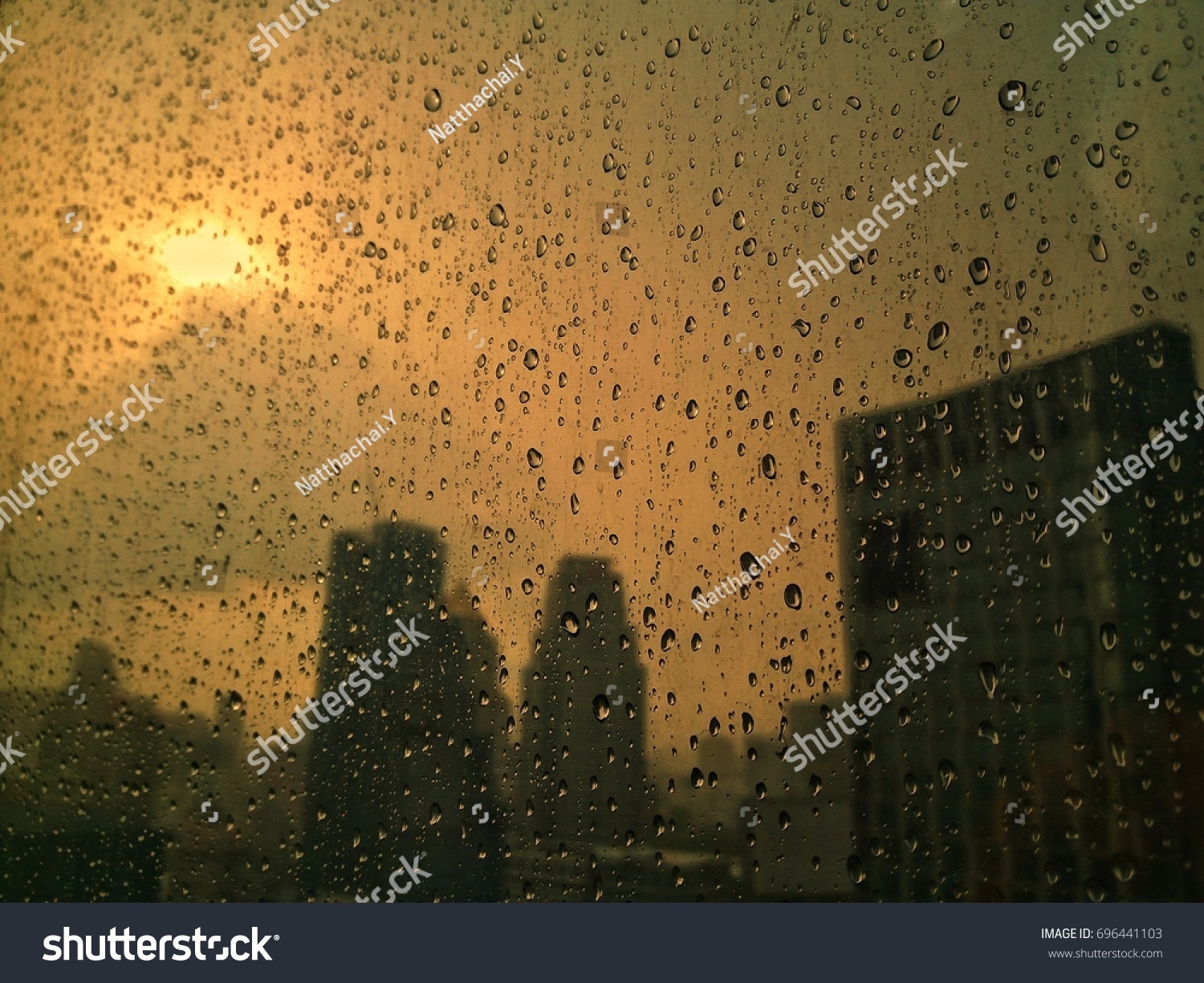 Raindrops on glass window and city background with sunshine in evening #696441103
