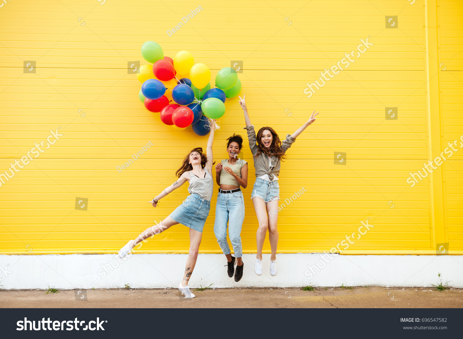 Picture of young happy women friends standing over yellow wall. Have fun with balloons.