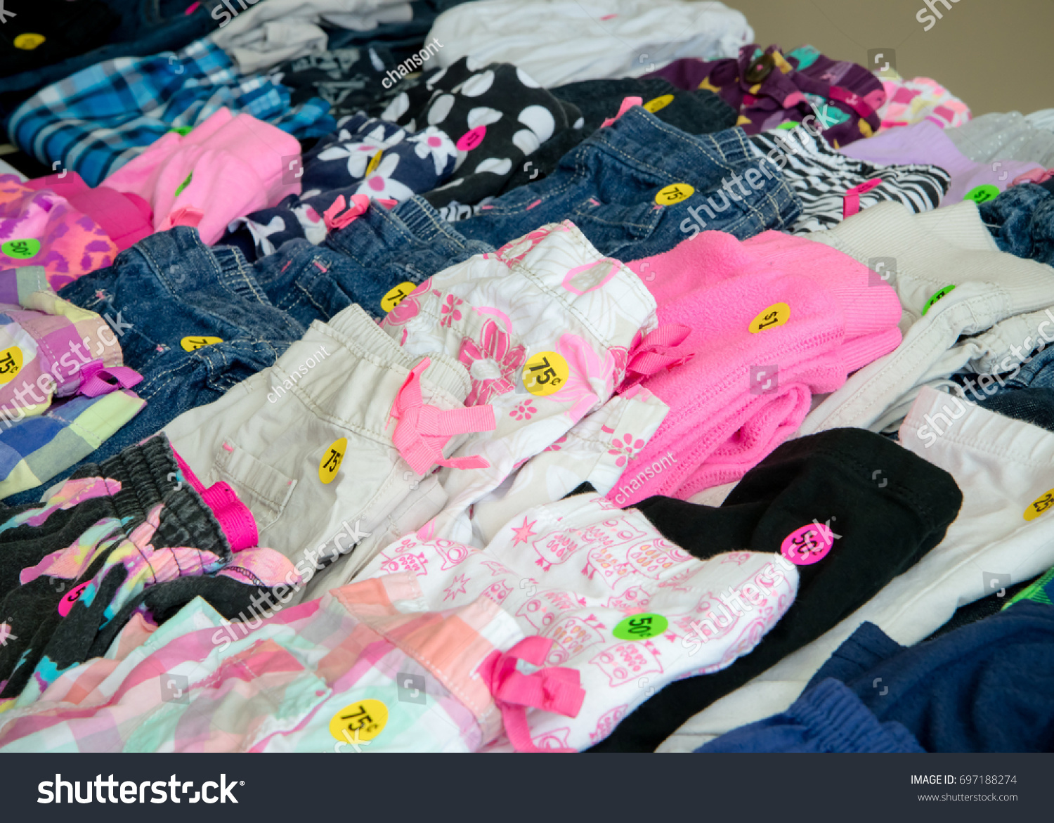 Colorful kids' clothing with price tags arranged on a garage sale table #697188274