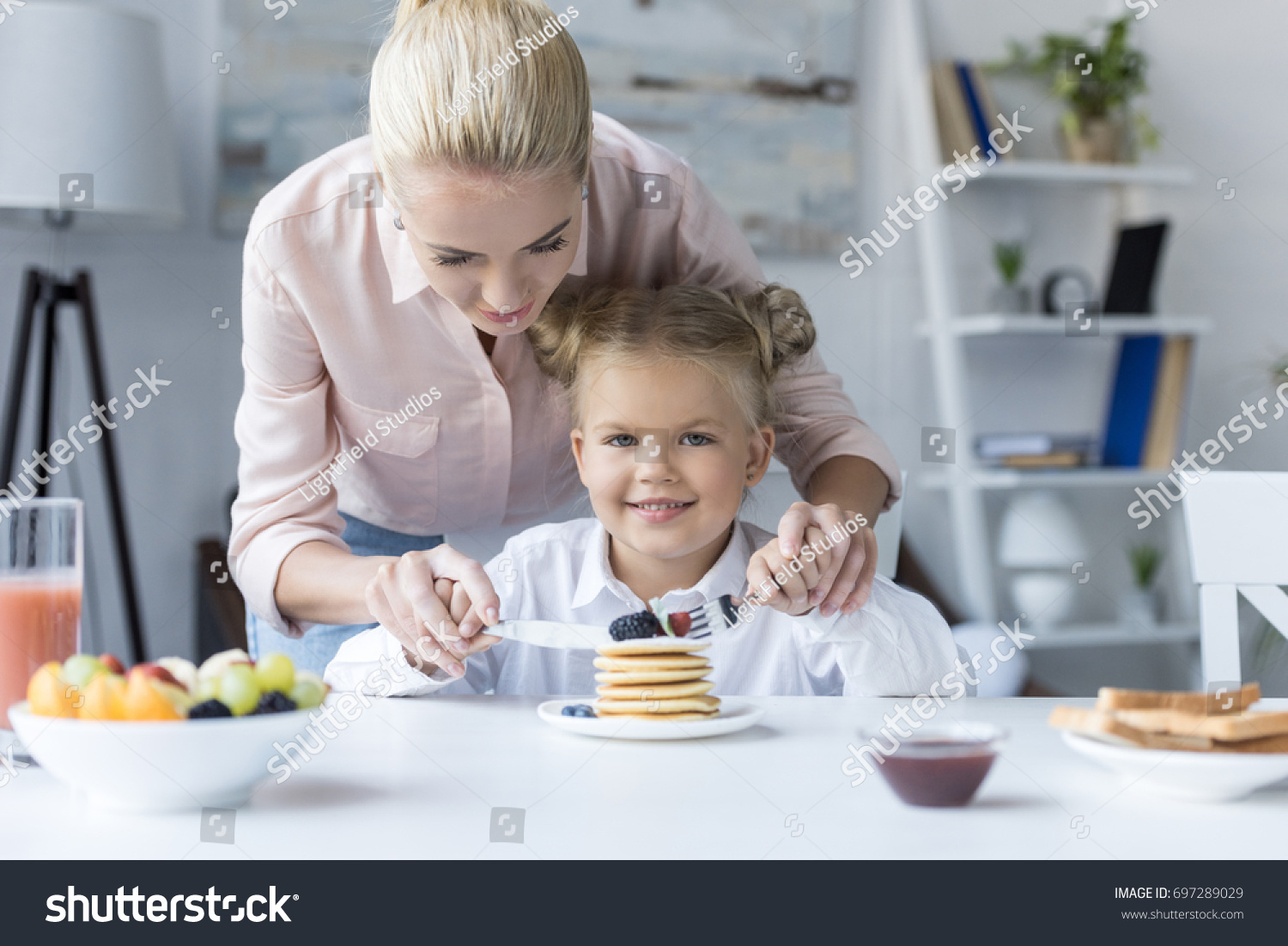smiling young mother with cute little daughter eating pancakes for breakfast #697289029