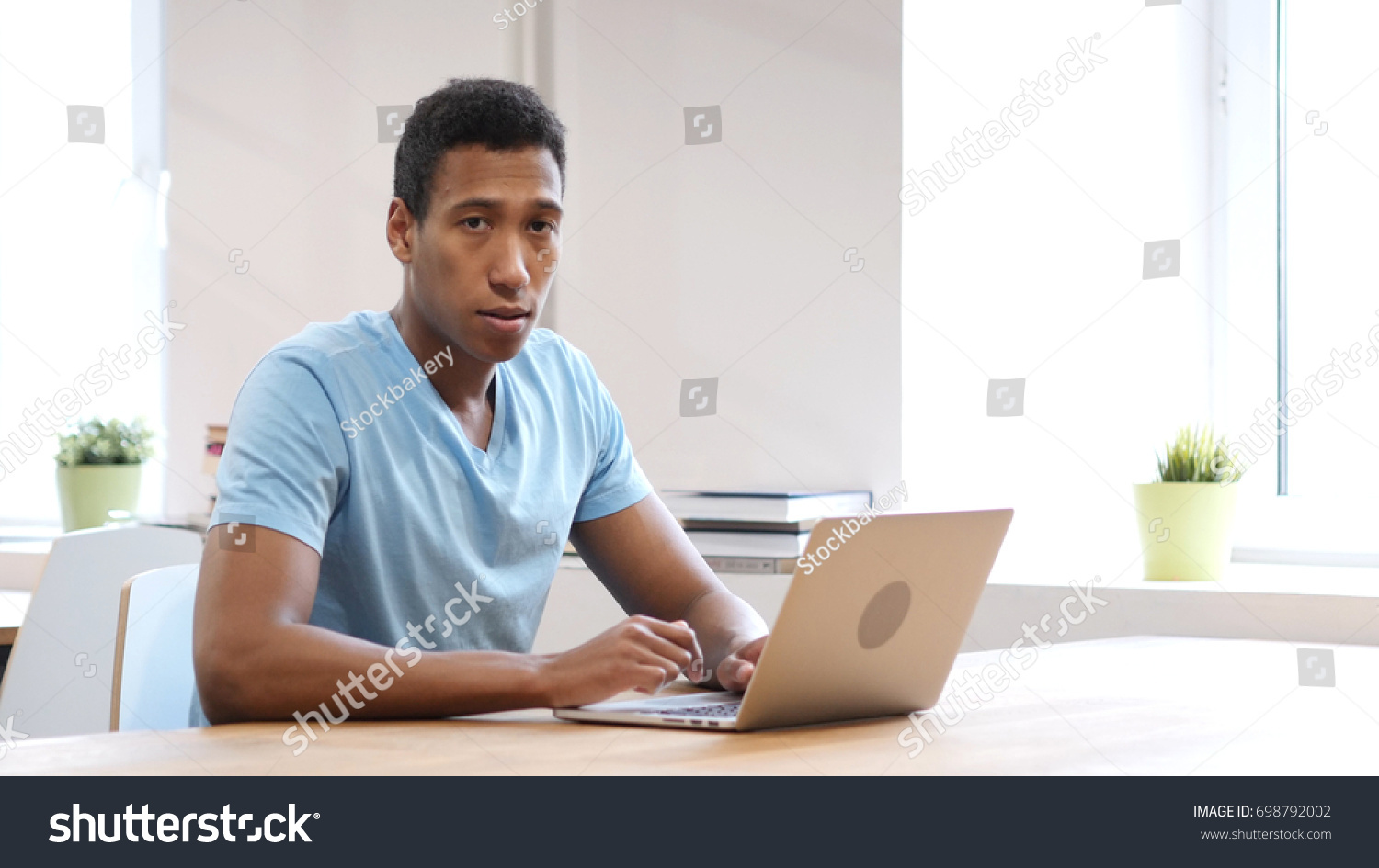 Serious Black Man Looking Toward Camera, Working on Laptop #698792002