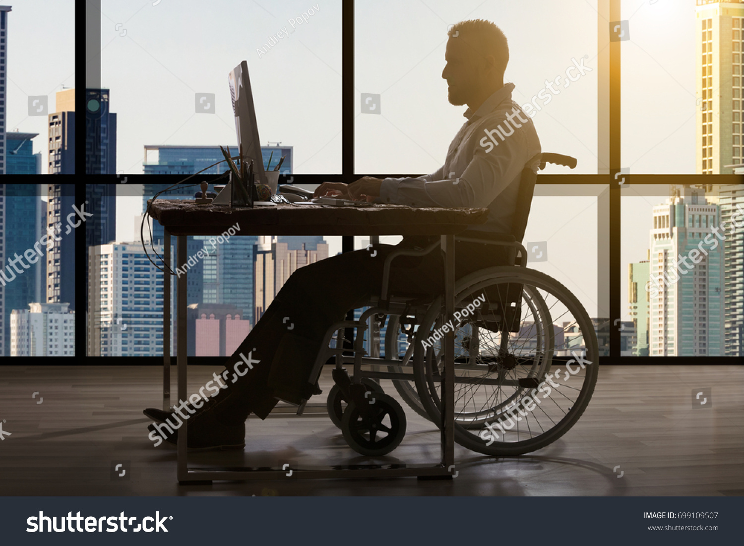 Disabled Businessman Sitting In Wheelchair Using Computer At Workplace #699109507