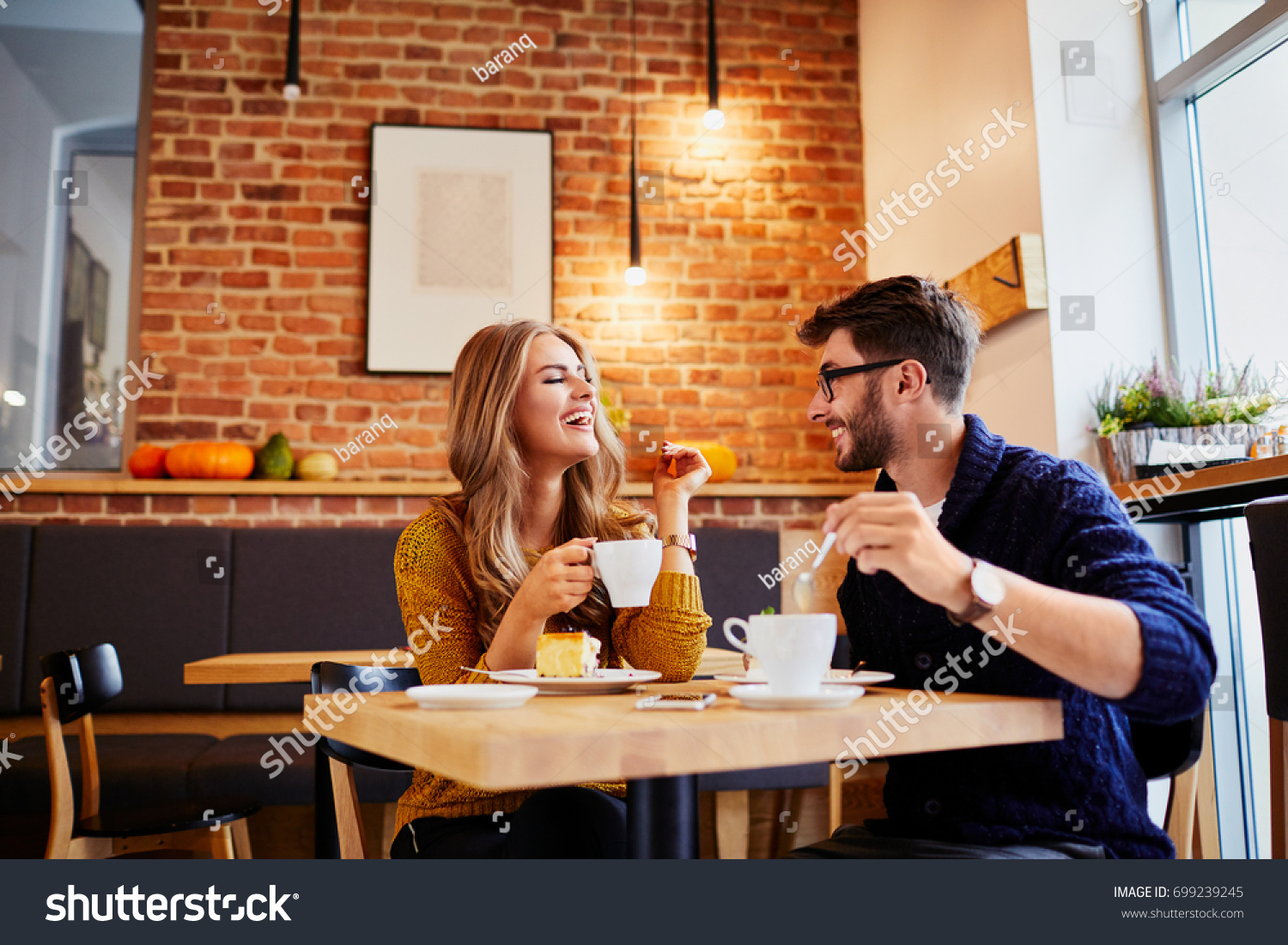 Couple of young people drinking coffee and eating cake in a stylish modern cafeteria #699239245