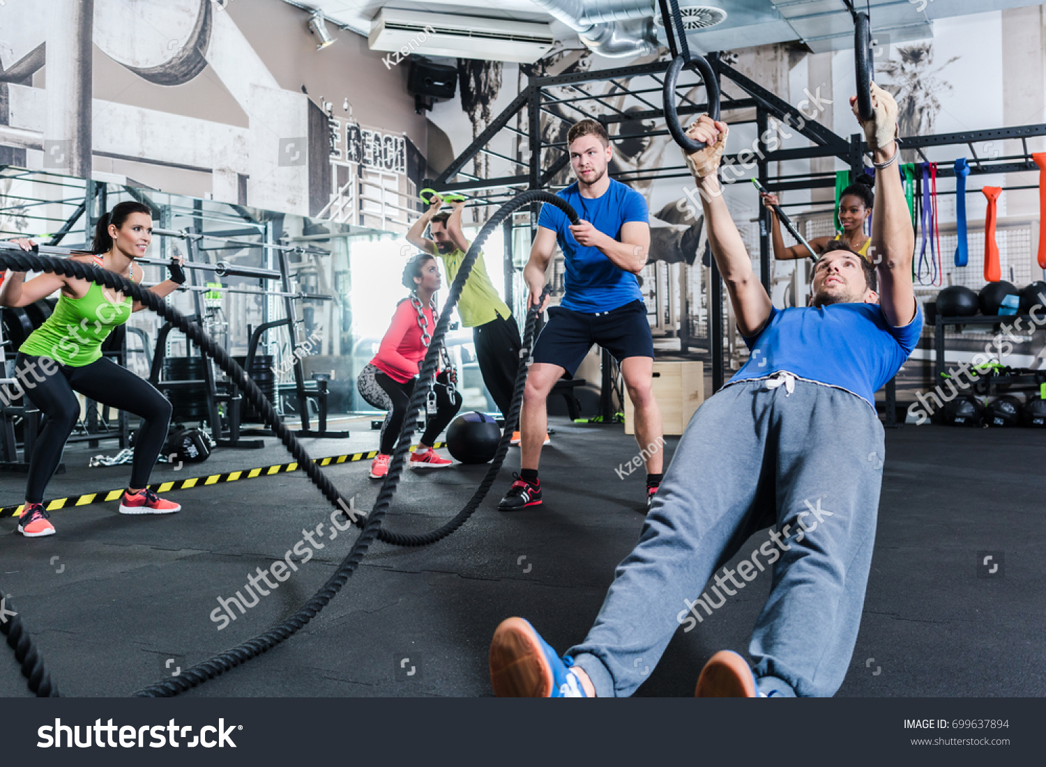 Men and women at functional fitness training in gym doing sport on rings and rope #699637894