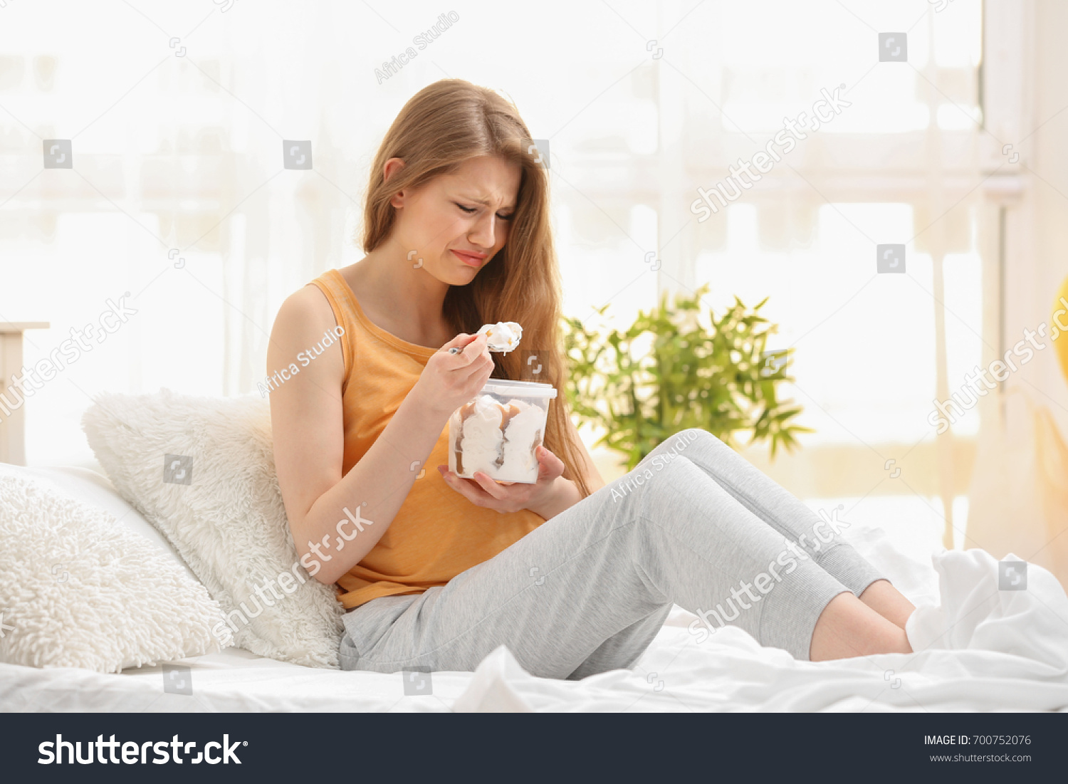 Emotional pregnant woman eating ice-cream in light room. Pregnancy hormones concept #700752076