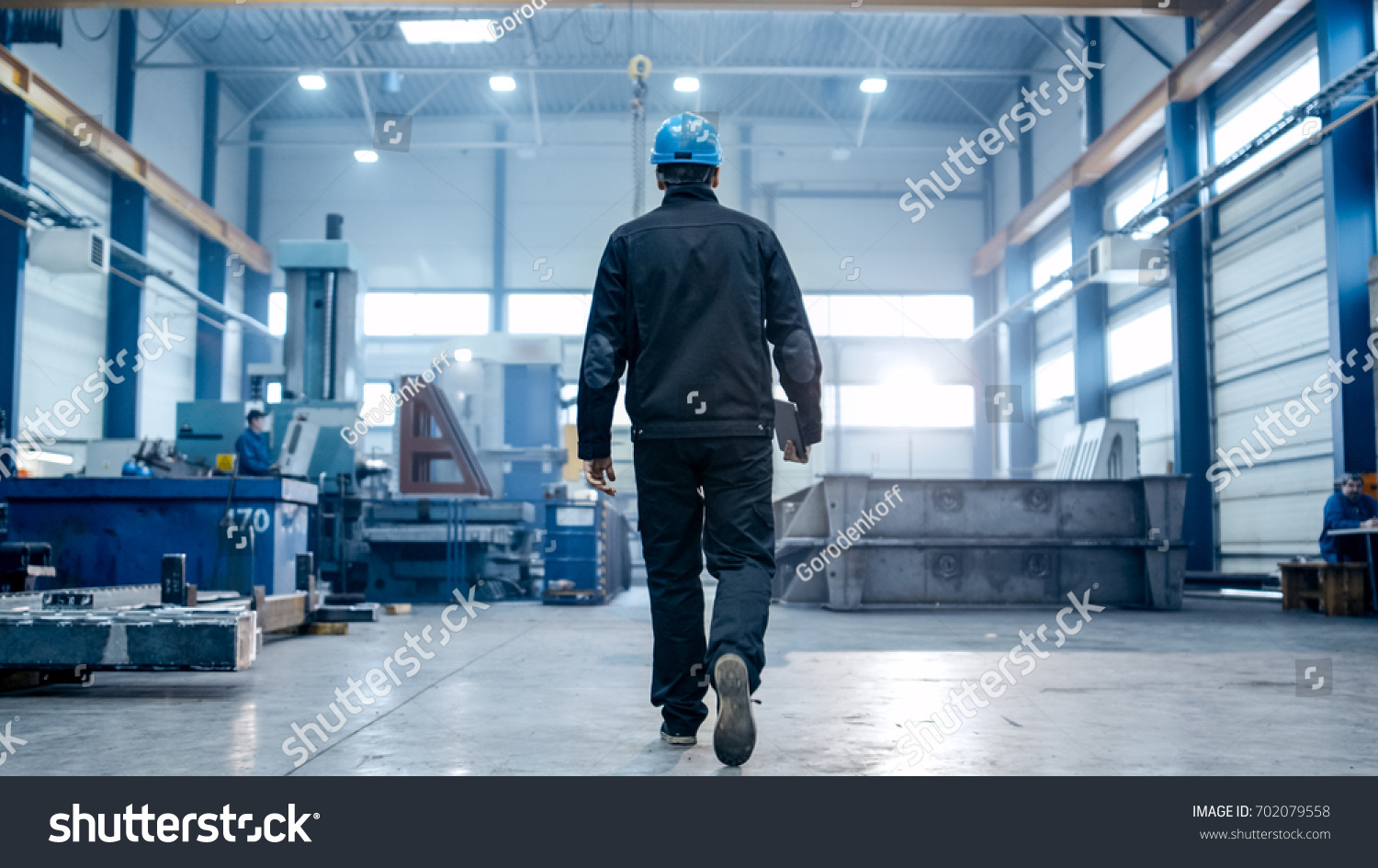 Factory worker in a hard hat is walking through industrial facilities. #702079558