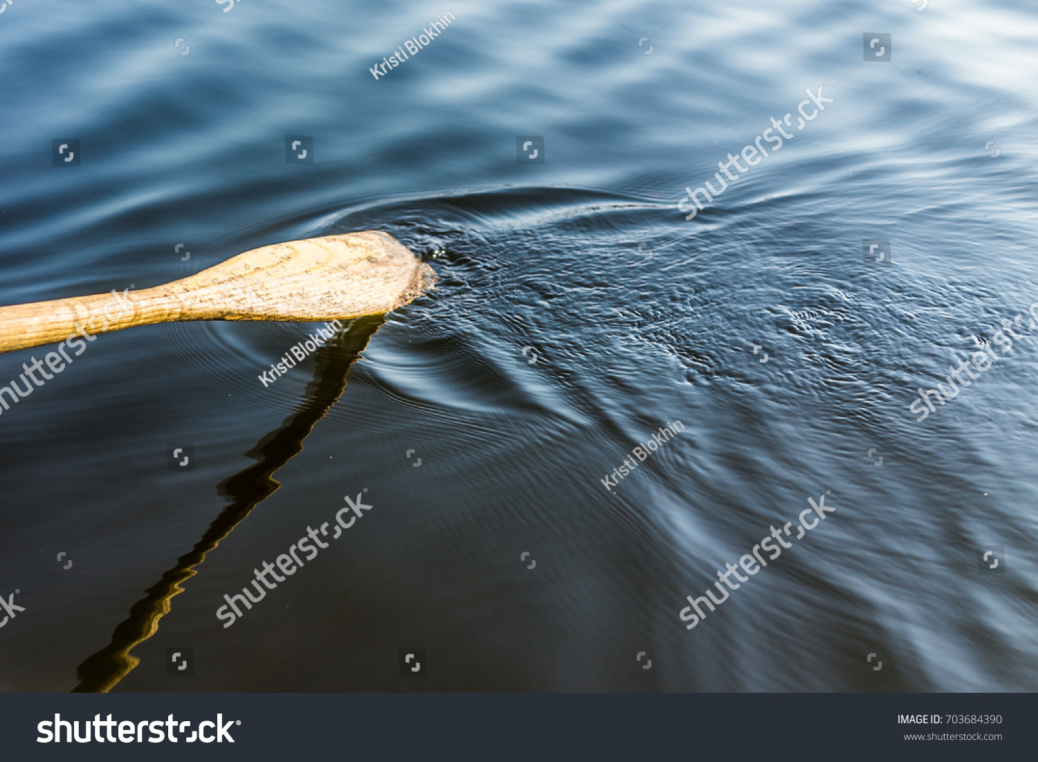 Closeup of oar paddle from row boat moving in water on green lake with ripples #703684390