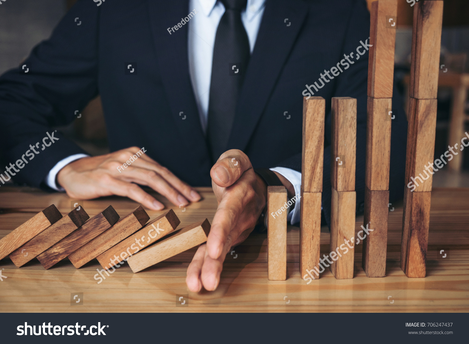 Close up of businessman hand Stopping Falling wooden Dominoes effect from continuous toppled or risk, strategy and successful intervention concept for business. #706247437