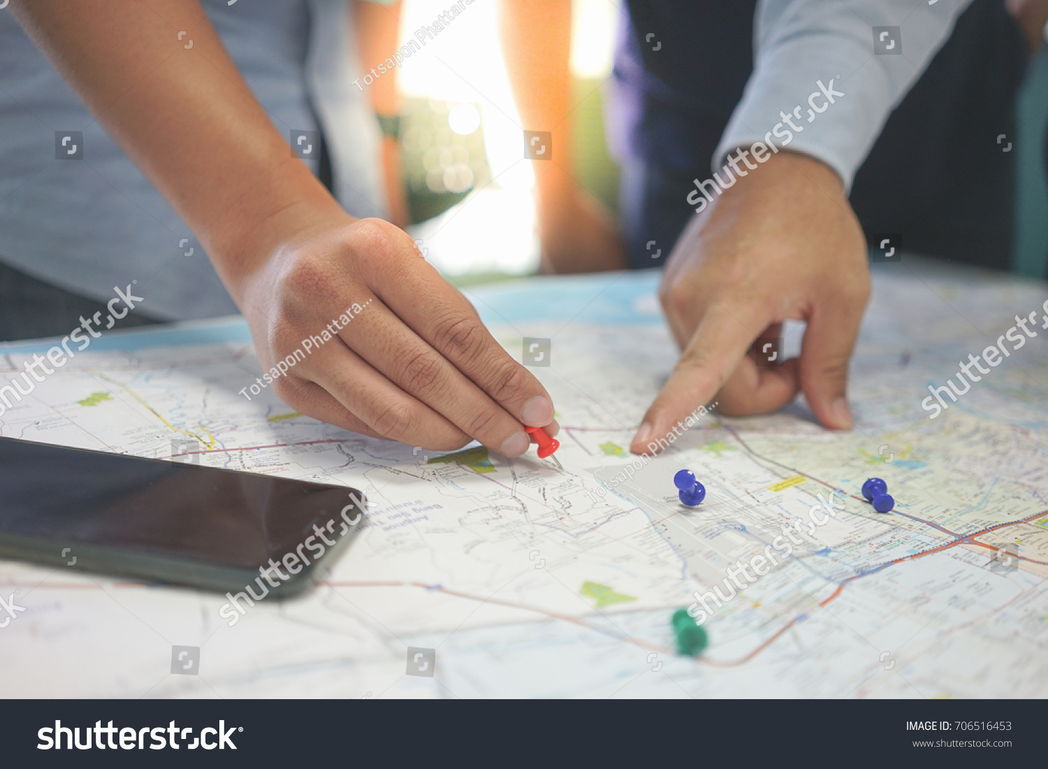 Two businessmen are talking about the target customer in the map. They hold pin in the hand and pointing finger to the area in the map. #706516453