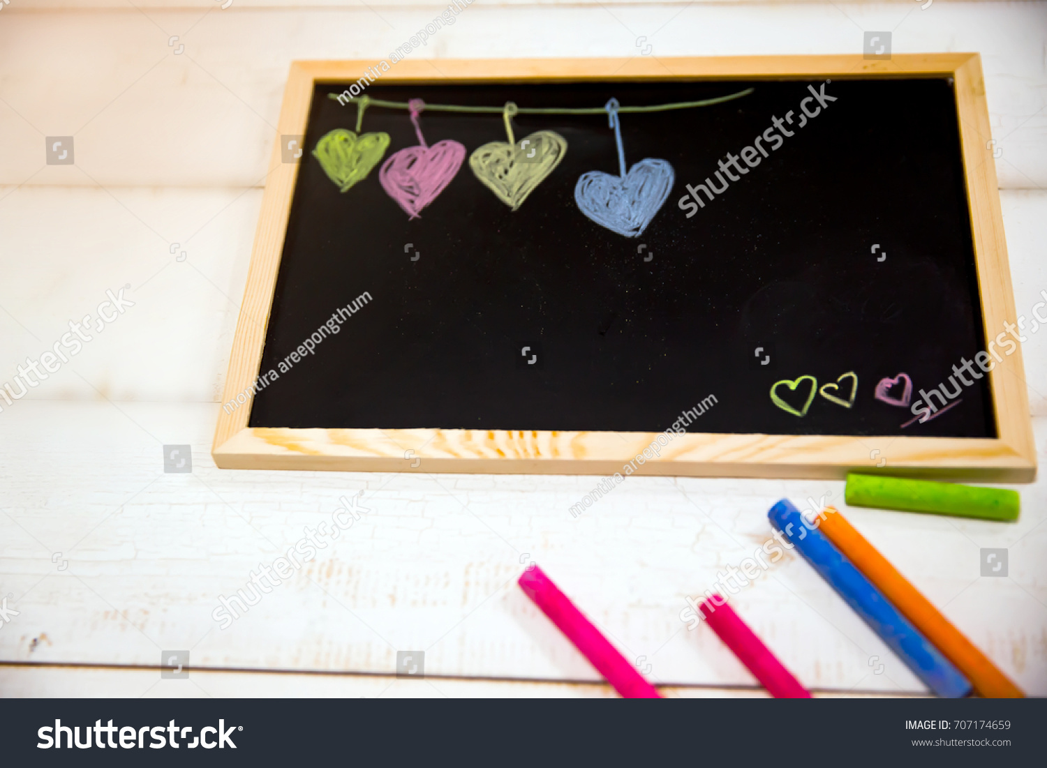 Cartoon heart draw by colorful chalk on wooden blackboard. blackboard and colorful chalk put on white table,  #707174659