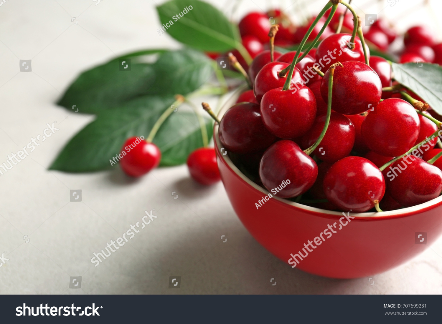 Ripe cherries in red ceramic bowl on light background #707699281