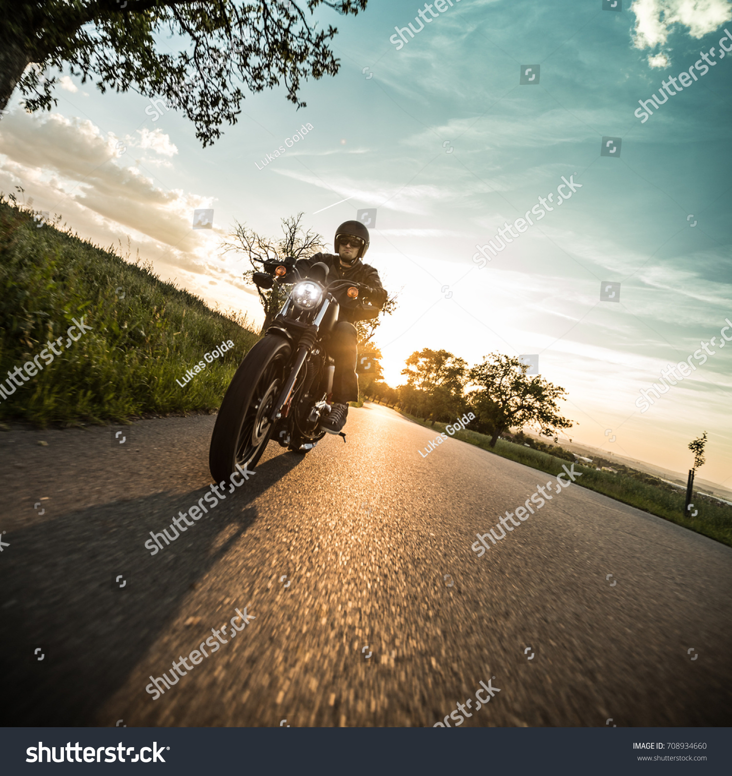 Man riding sportster motorcycle on countryside during sunset. #708934660