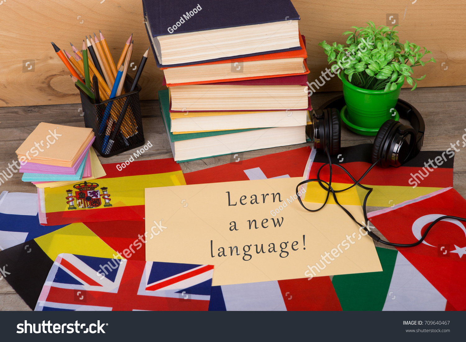 Learning languages concept - paper with text "Learn a new language!", flags, books, headphones, pencils on wooden background #709640467