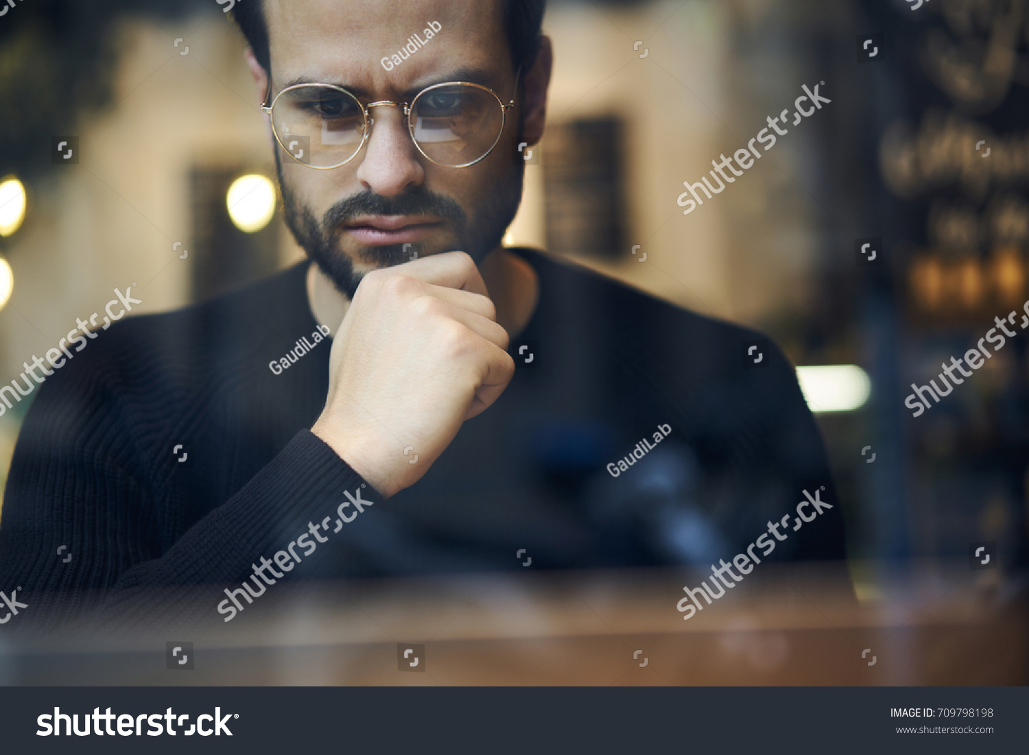 Cropped close up image of pensive bearded entrepreneur in optical spectacles for better views dressed in black sweatshirt.Pondering businessman in trendy eyeglasses thinking on blurred background #709798198