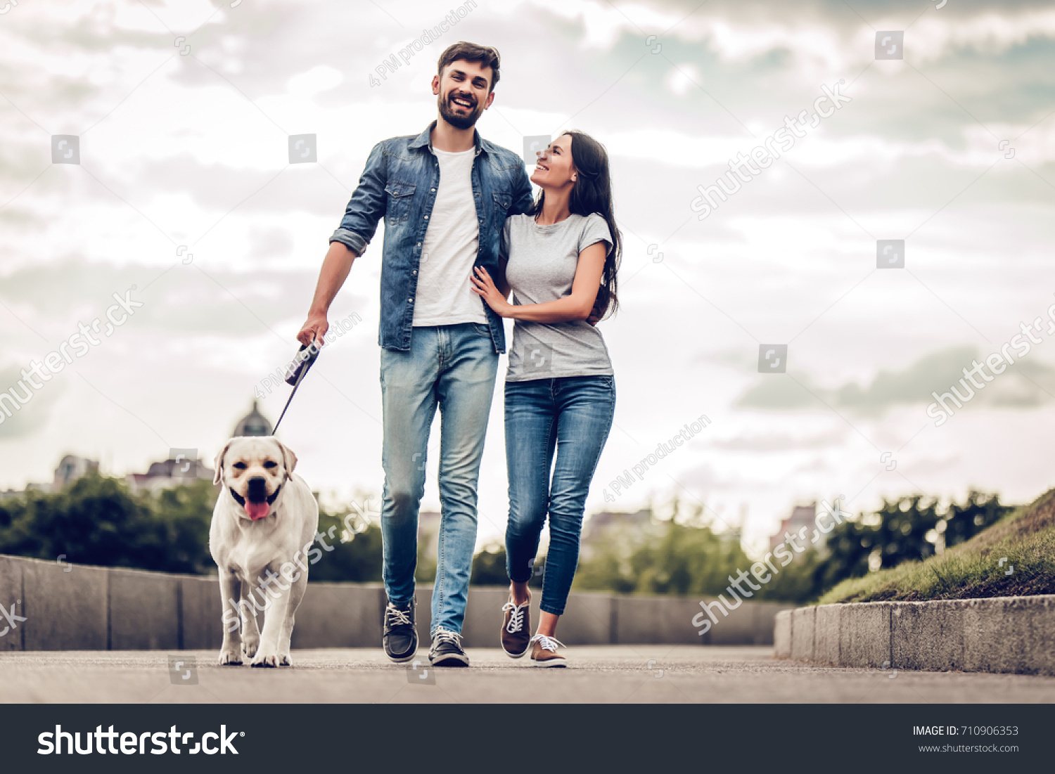 Romantic couple is on a walk in the city with their dog labrador. Beautiful young woman and handsome man are having fun outdoors with golden retriever labrador. #710906353
