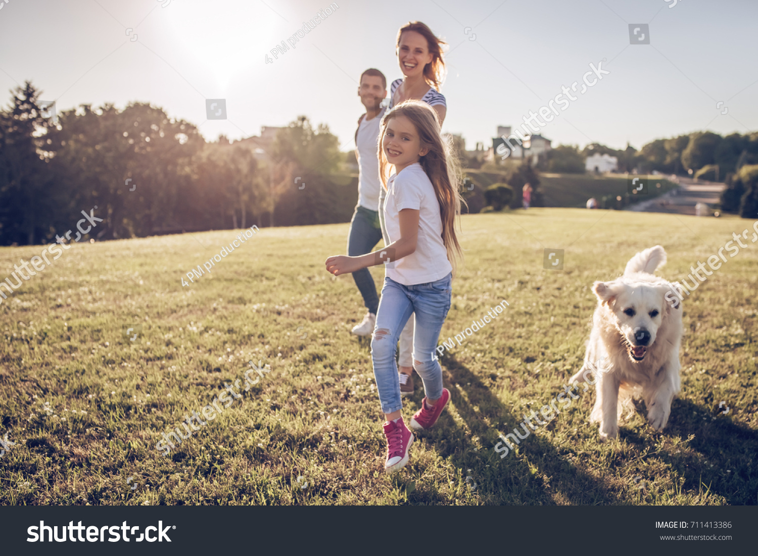 Beautiful happy family is having fun with golden retriever outdoors. Mother, father and daughter are running with dog labrador in park. #711413386