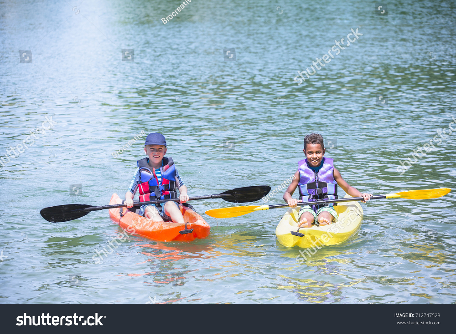 Two smiling cute diverse boys kayaking together on the lake. Having fun in the summertim #712747528