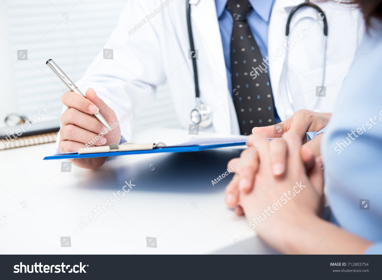 Male doctor noting a female patient medical check up information in hospital #712803754