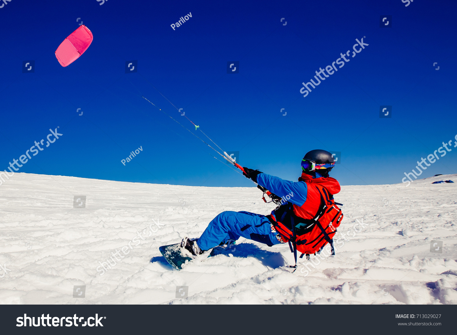 Snowboarder with a kite on fresh snow in the winter in the tundra of Russia against a clear blue sky. Teriberka, Kola Peninsula, Russia. Concept of winter sports snowkite. #713029027