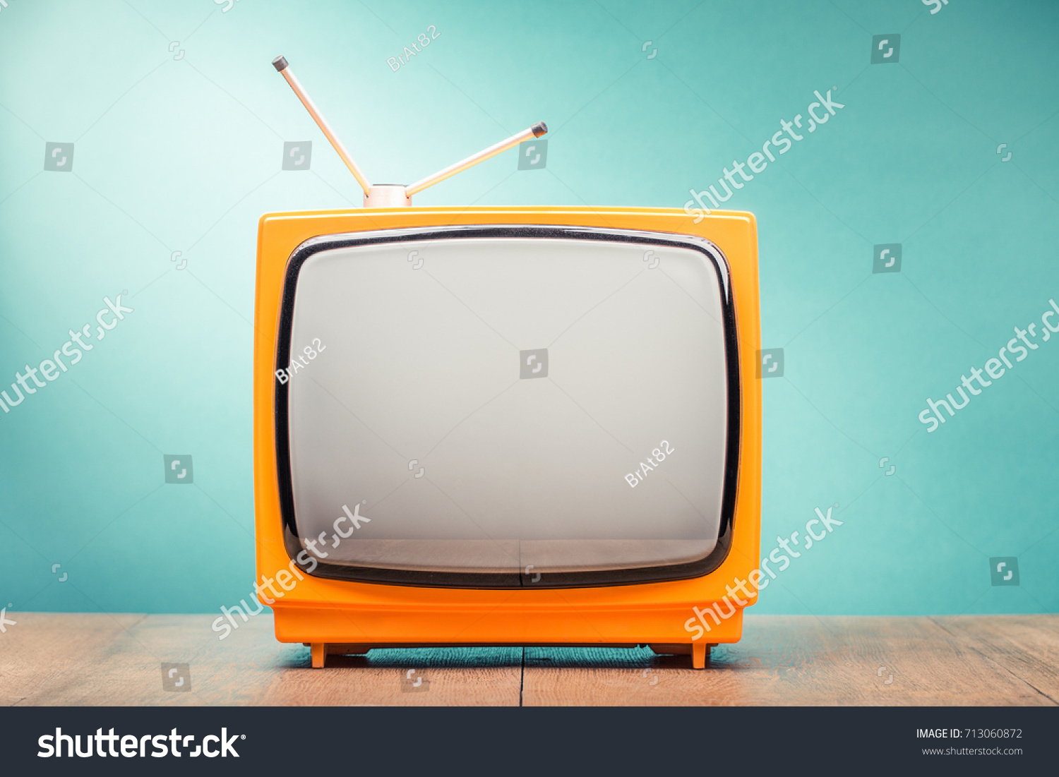 Retro old orange TV set receiver on wooden table front gradient mint green wall background. Vintage instagram style filtered photo #713060872