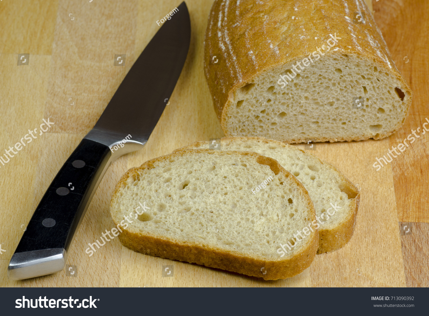 Close-up photo of two slices of bread cut by knife with black handle on a wooden board table with blurred background #713090392
