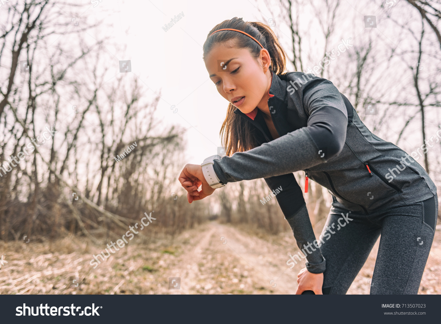 Sport watch run woman checking smartwatch tracker. Trail running runner girl looking at heart rate monitor smart watch in forest wearing jacket sportswear. Female athlete jogger training in woods. #713507023