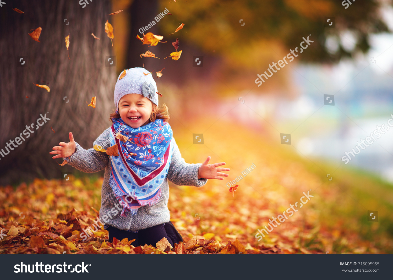 adorable happy girl playing with fallen leaves in autumn park #715095955
