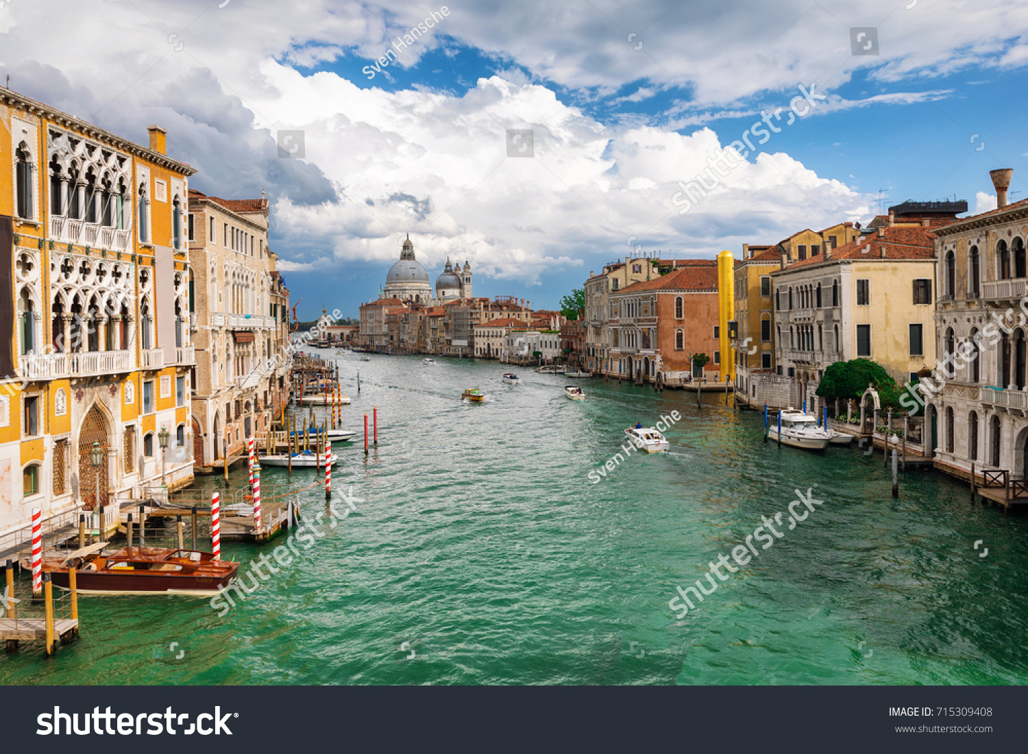 View to the Basilica di Santa Maria della Salute and Canale Grande in Venice, Italy, during a cloudy summer day #715309408
